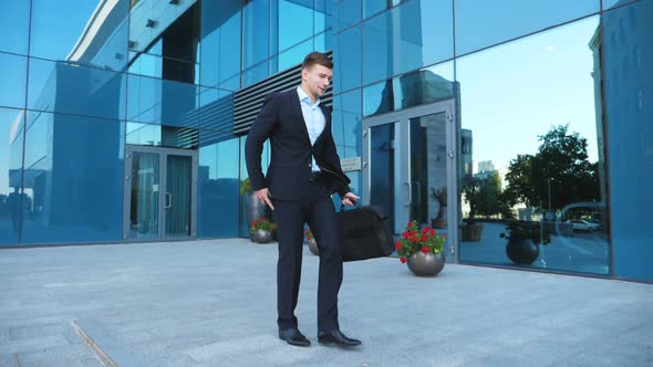 Young Happy Businessman in Suit Walks Along City Street and Jumps Celebrating Achievement