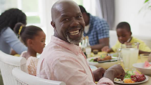 Happy african american grandfather eating lunch with family at home