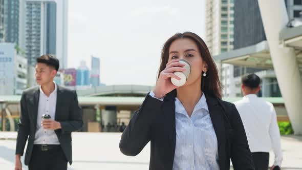 Asian young smart business woman holding a cup of coffee, using smartphone in city with confidence.