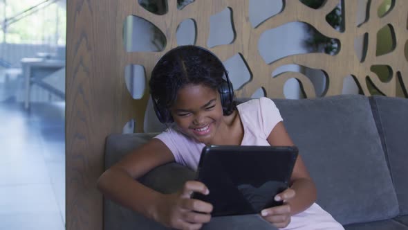 African american girl smiling while using digital tablet sitting on the couch at hospital