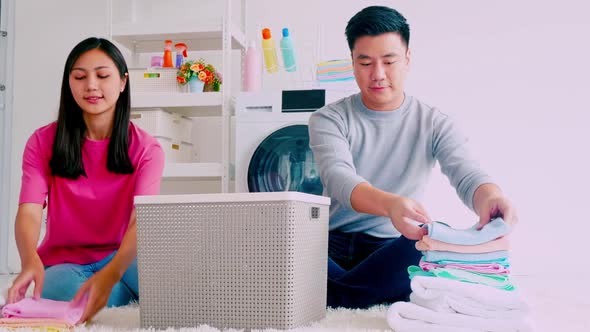 Husband helping his wife folding clothes. Happy Asian couple spending time together at home.