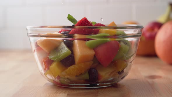 Camera follows pouring sauce over fruit salad. Slow Motion.