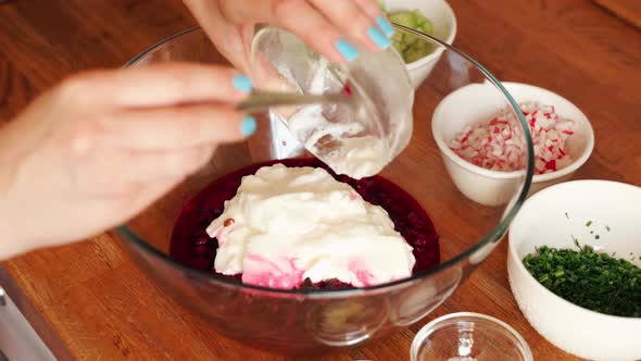 Woman Prepares Cold Beetroot Soup in Glass Bowl on Wooden Table