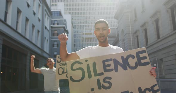 Two mixed race men on a protest march holding placards raising hands and shouting