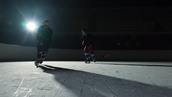 Two Sportsmen Hockey Players Who are Sliding on Ice Arena and Dribbles Hitting Puck with Stick