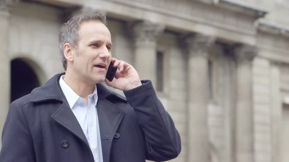 Business man stands a amidst a busy square whilst taking a business call