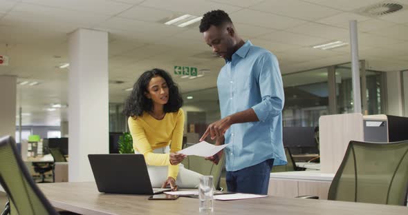 Video of happy diverse businessman and businesswoman using laptop, talking about project