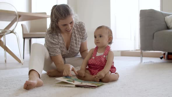 Cheerful Mother and Daughter Sitting on Floor Reading Book