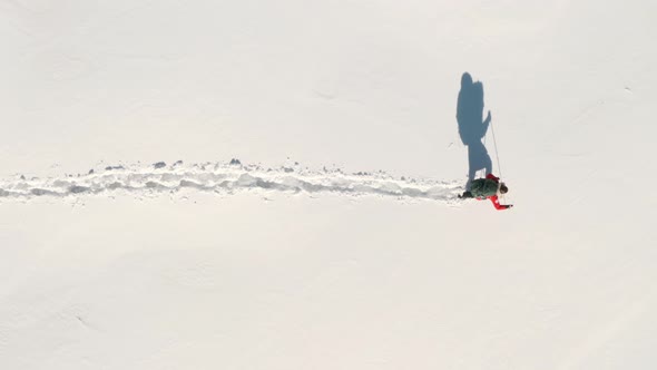 Top down aerial shot of adventurous man walking through deep snow with large trekking bag