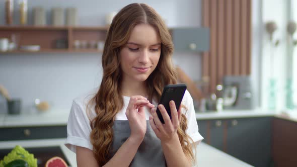 Pretty Woman Using Phone in Kitchen. Happy Housewife Preparing Cooking at Home