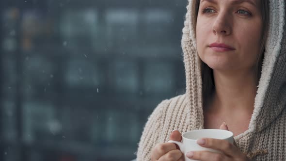 Woman Stays on Balcony During Snowfall with Cup of Hot Coffee or Tea