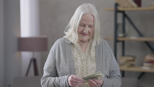 Greyhaired Old Caucasian Woman Counting Money Sighing Looking at Camera