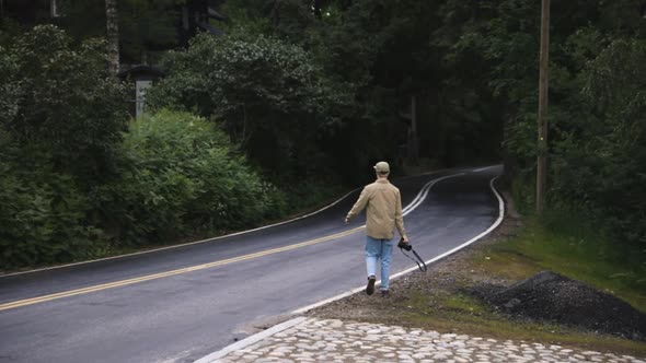 Young male photographer walks on country road by forest, slow pan