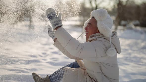 A Gay Gay Man in Warm Clothes Sits in the Snow in Winter and Plays and Enjoys a Sunny Day