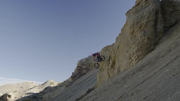 Slow motion of guy riding mountain bike off rocky cliff down a steep rocky slope.