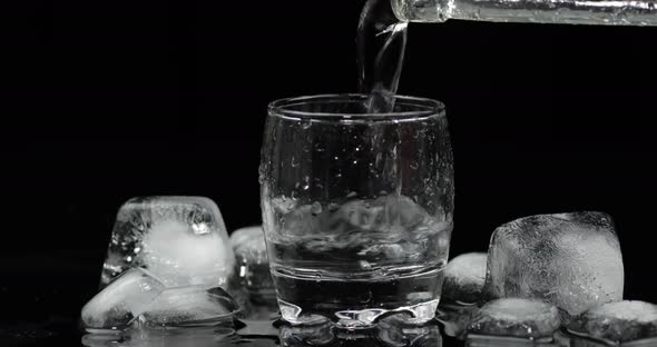 Pouring Up Shot of Vodka From a Bottle Into Glass. Black Background