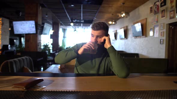 a Bearded Man Is Sitting in a Bar Drinking Whiskey and Talking on the Phone