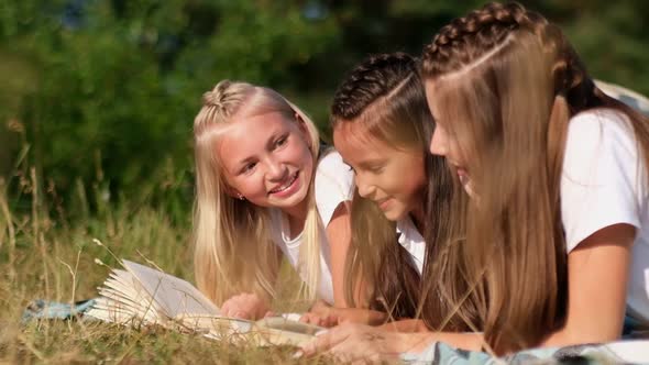 Teenage Girls are Reading a Book Lying on the Green Grass They are Having Fun at a Summer Camp