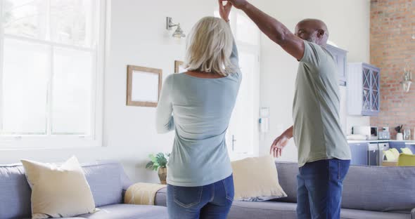 Mixed race senior couple dancing together in the living room at home