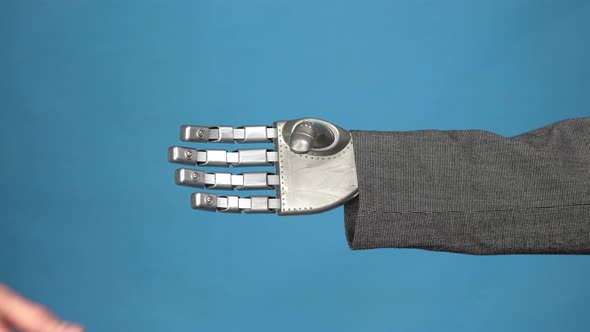 A Young Man Shakes the Gray Mechanical Arm of a Cyborg. Handshake of Two Businessmen. Hands Closeup