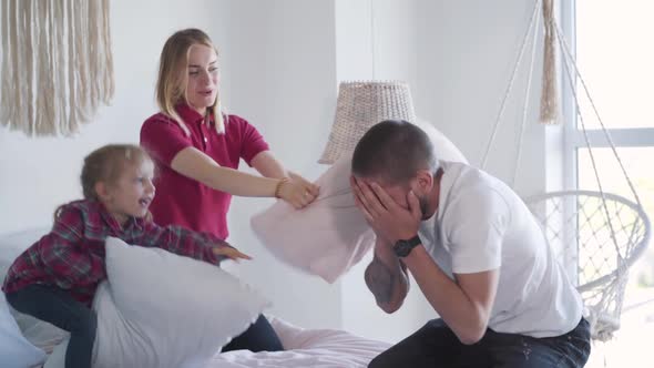 Happy Family Fighting Pillows in Bedroom. Laughing Young Man, Woman and Little Joyful Girl Having