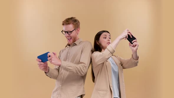 A Young Coupple Playing Games on Mobile Phone Isolated Over Beige Background Positive and Negative