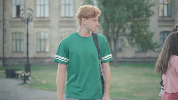 Unhappy Redhead Young Man Passing Group of Laughing Groupmates on Campus. Portrait of Bullied