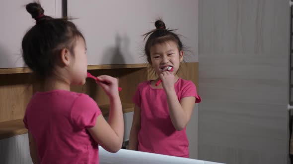 Cute Asian Girl Brushing Teeth at Bathroom Mirror