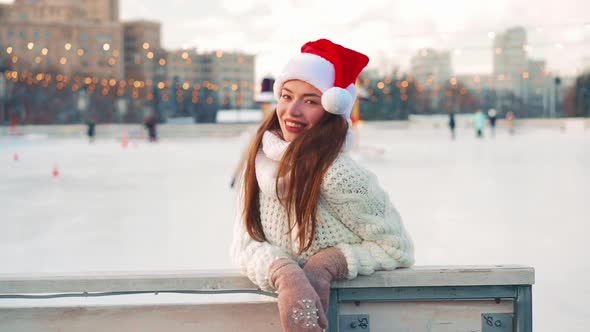 Young Smiling Woman Santa Hat Ice Skating Outside on Ice Rink Dressed White Sweater