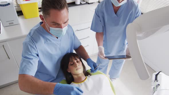 Caucasian male dentist with face mask examining teeth of female patient at modern dental clinic