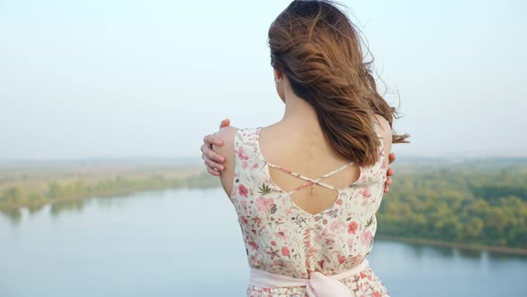 Attractive Woman with Loose Hair Hugs Shoulders on Riverbank
