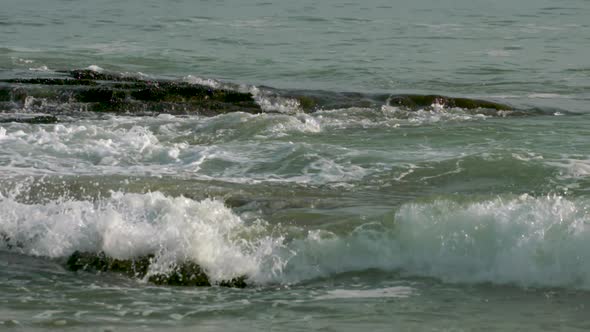 Slow motion footage of waves crashing against rocks as they roll into shore