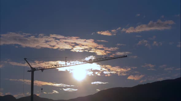 Time lapse shot of flying clouds against blue sky and silhouette of crane in sunset