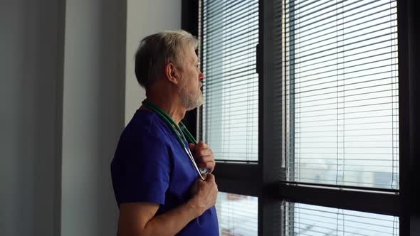 Tracking Shot of Thoughtful Mature Male Doctor Looking Outside Through Window Looking Away