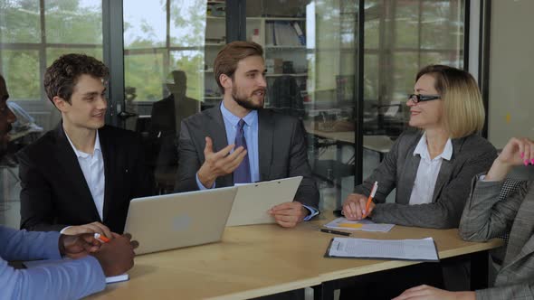 Businessman in Suit Talking to Businesspeople Colleagues Sitting at the Table