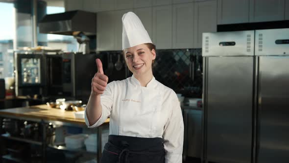 Professional kitchen portrait: Female Chef showing thumbs up and smiling