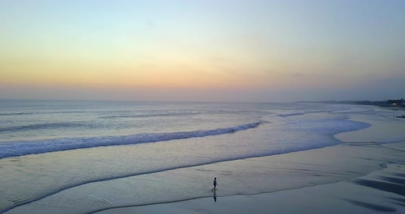 Aerial drone view of a young woman walking on the beach at sunset