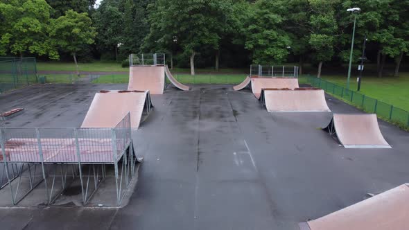 Aerial view flying reverse above fenced skate park ramp in empty closed public playground