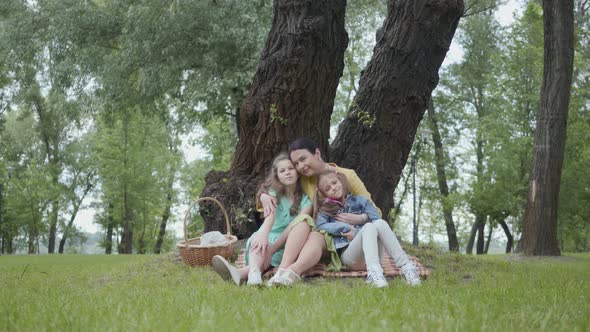 Portrait Senior Cute Woman Kissing and Hugging Adorable Granddaughters Sitting on the Grass