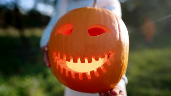 Child Holding Carved Smiling Happy Pumpkin on Sunny Garden Background