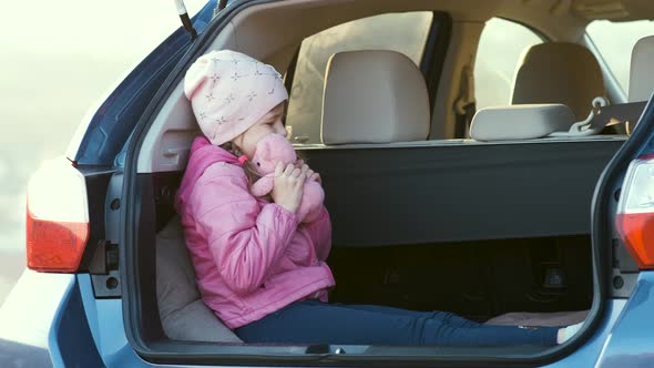 Pretty Happy Child Girl Playing with a Pink Toy Teddy Bear in a Car Trunk