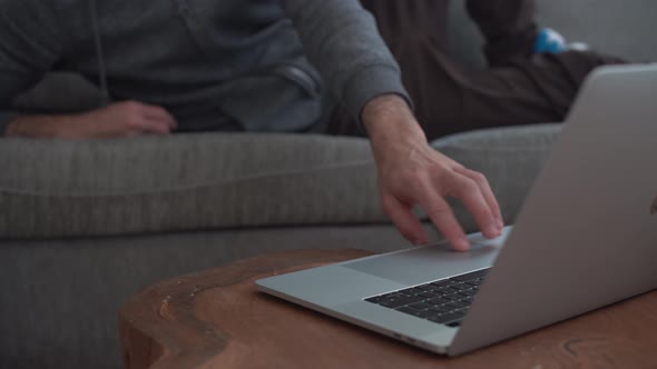 Guy lying on sofa types on his laptop at home