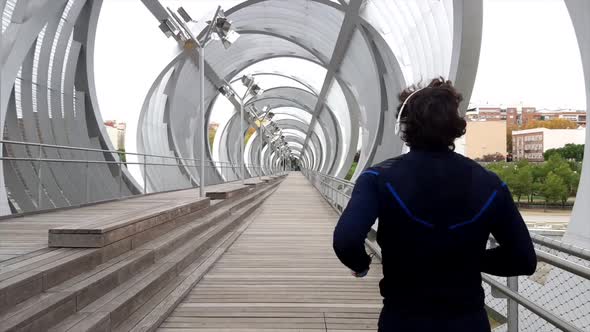 Unrecognizable sportsman in active wear jogging over outdoors bridge