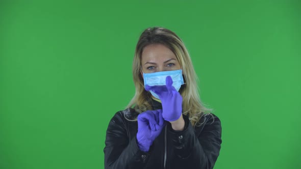 Portrait of Beautiful Young Woman in Medical Mask Is Looking at Camera and Puts on Rubber Gloves