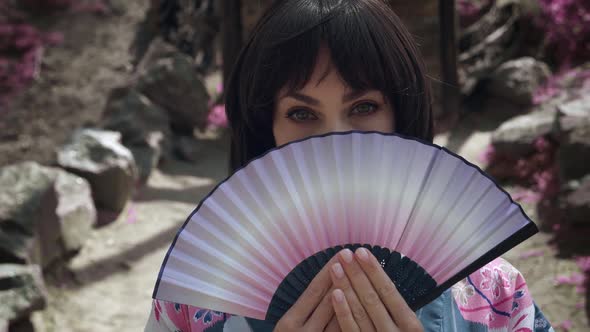 Closeup of Caucasian Geisha Woman in Traditional Japanese Kimono is Covering Her Face with Wooden