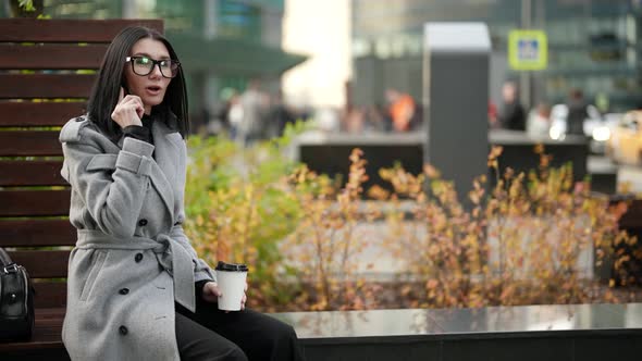 Woman is Waiting Someone in Park and Calling By Mobile Phone Holding Carton Cup of Coffee