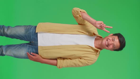 A Smiling Young Asian Man Showing Gesture Peace While Standing On Green Screen In The Studio