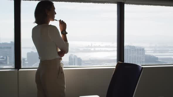 Back view of caucasian businesswoman standing at window and thinking