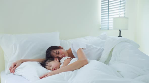 Asian mother turn off the light and lying down with daughter on bed. Activity relationship concept.