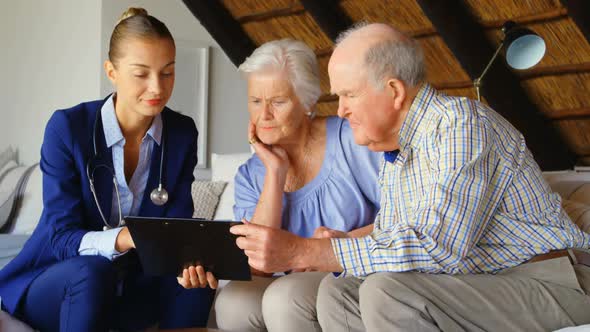 Front view of Caucasian senior couple discussing over clipboard with female doctor at comfortable co